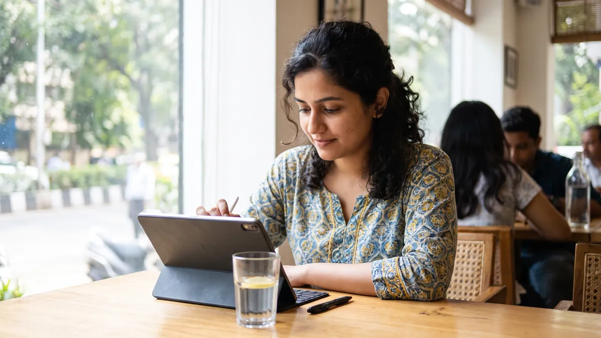 Close candid view of a woman in Mumbai reading a consent form on a tablet at a bright table, a pen and a glass of water nearby, her face in soft focus.